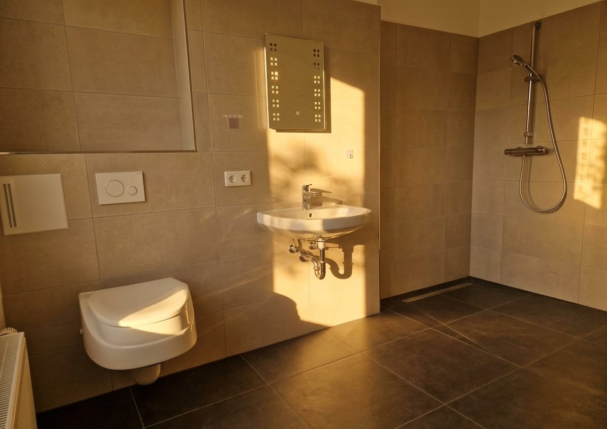 Helles Badezimmer mit bodengleicher Dusche, Waschbecken und Hänge-WC