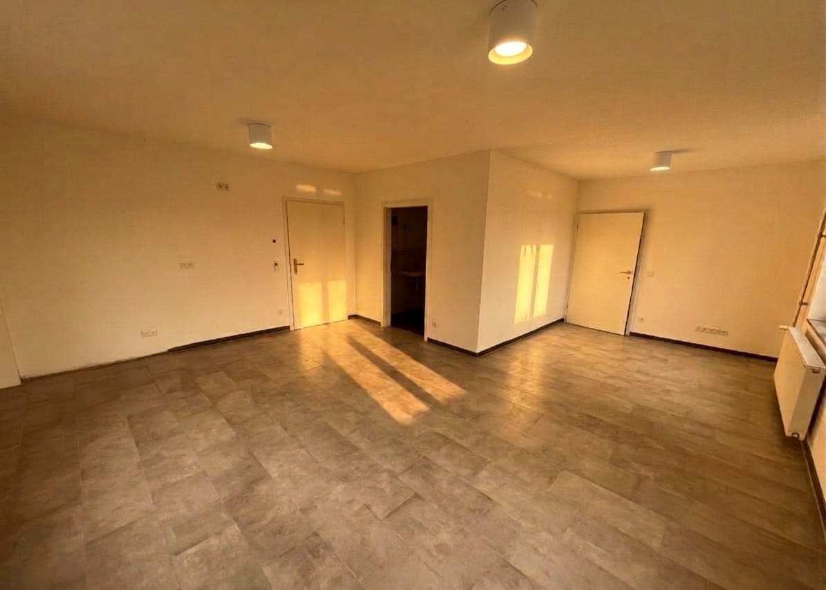 Heller, leerer Wohnraum einer Beispielwohnung im Abendlicht, mit Türen zu Bad und Schlafzimmer